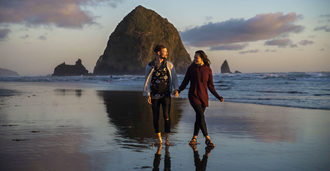 A couple walks along Cannon Beach, Oregon, on a romantic evening date.