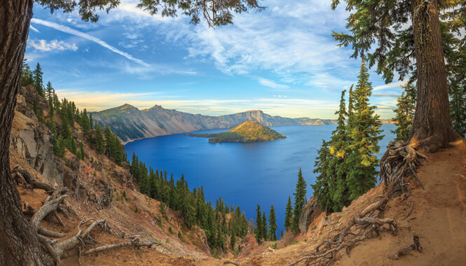 View of the blue water of Crater Lake from a hilltop framed with pines