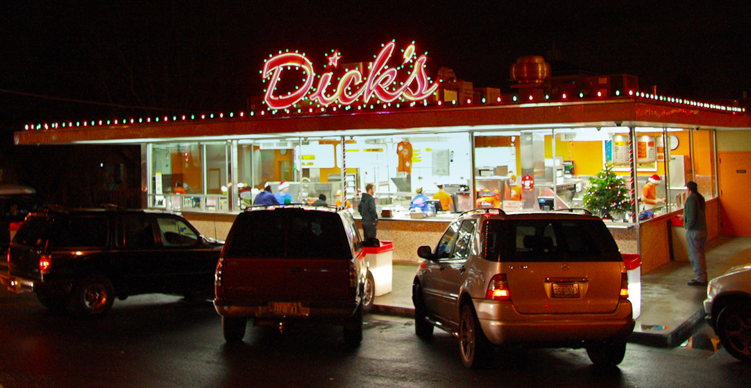 Picture of Dick's Drive In in Wallingford with a neon Dicks sign on the roof lighted up at night with cars parked outside