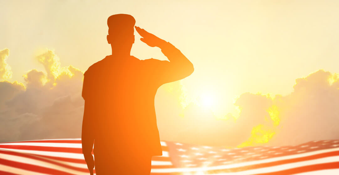 A solder back turned saluting the flag at sunset