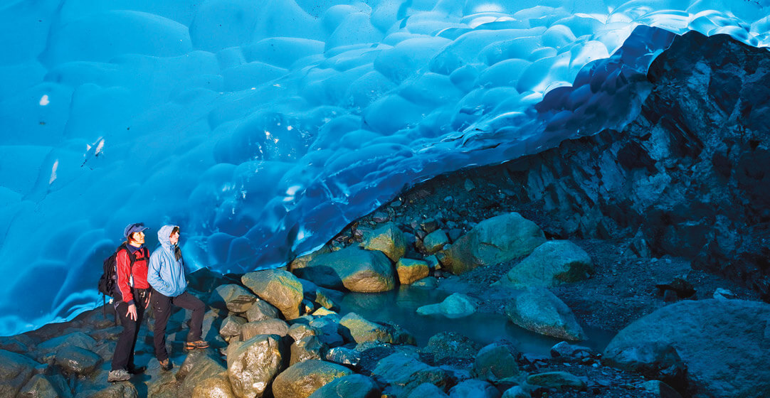 Two hikers standing at the edge of the blue ice sheet of the Mendenhall Glacier near Juneau