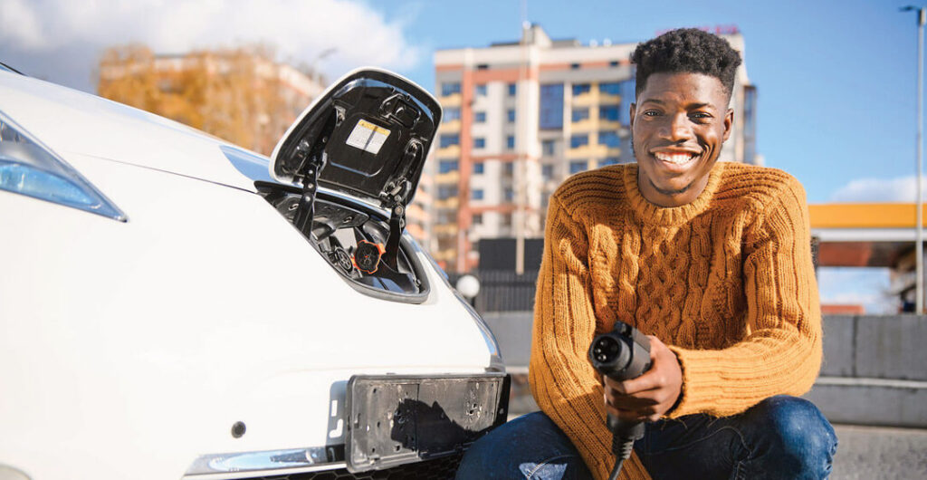 A young African American man smiles while his electric car charges