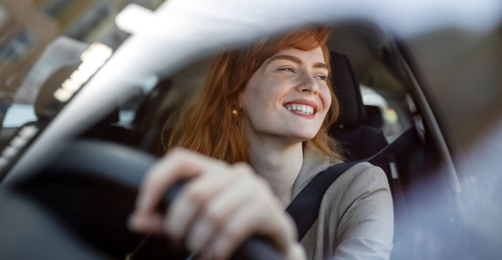 Happy young woman driving an electric car. What does it feel like to drive an electric car? Most electric cars feel close to high-performance sports cars in their handling.
