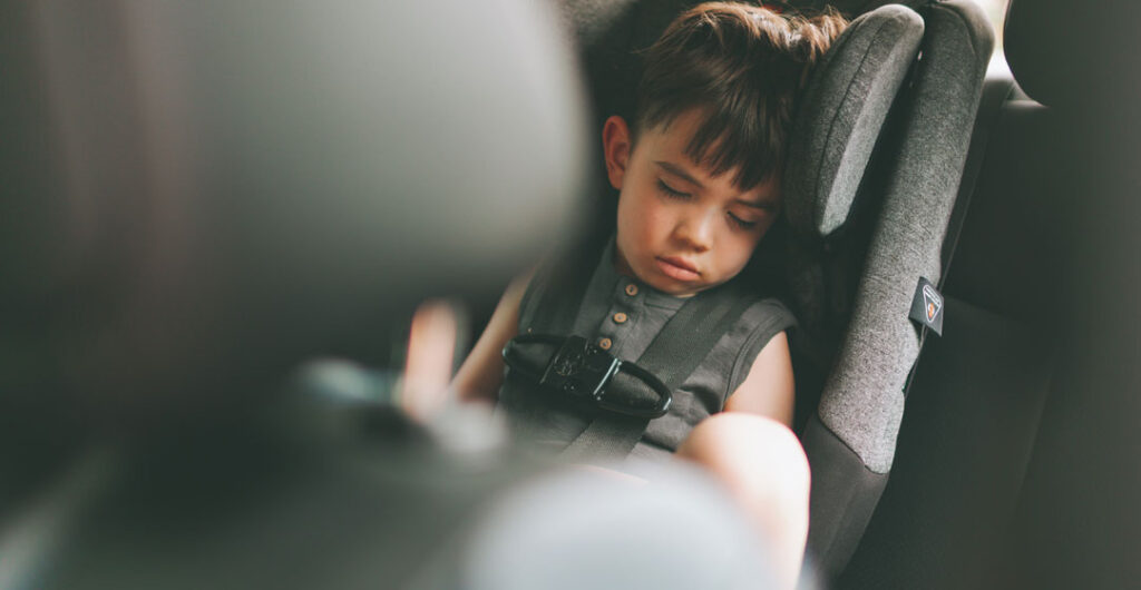 A boy toddler is sitting in a safety seat. 