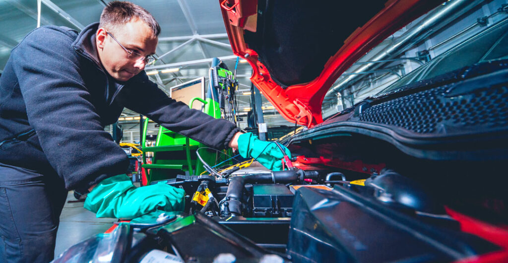 A mechanic works on an open hood. Electric car repairs are few and far between — compared to gas powered cars. 