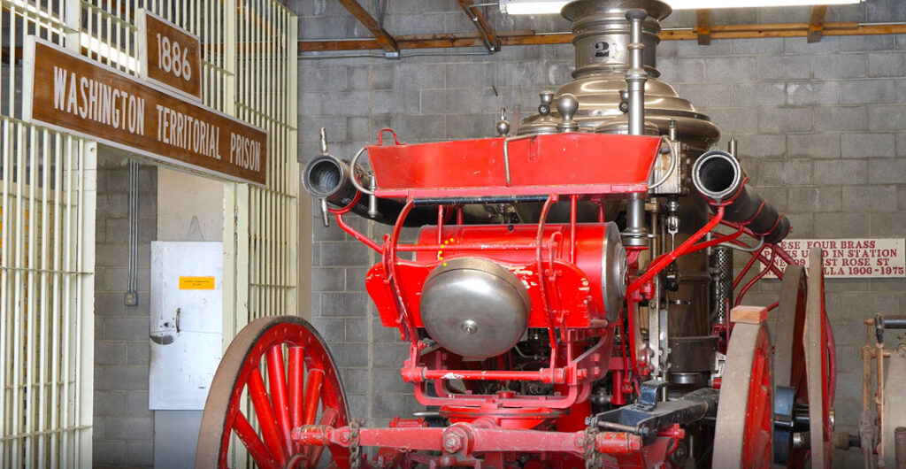 A red steam-powered buggy next to one of the cells at the Fort Walla Walla Museum. 