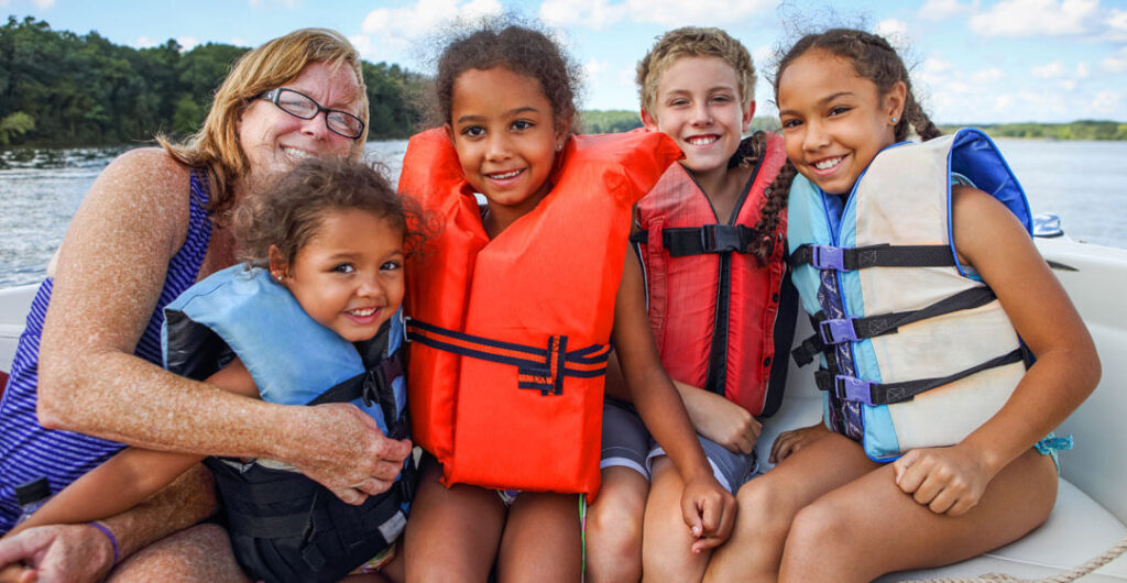 A family in life jackets on a boat on the lake to illustrate the importance of boat insurance. 