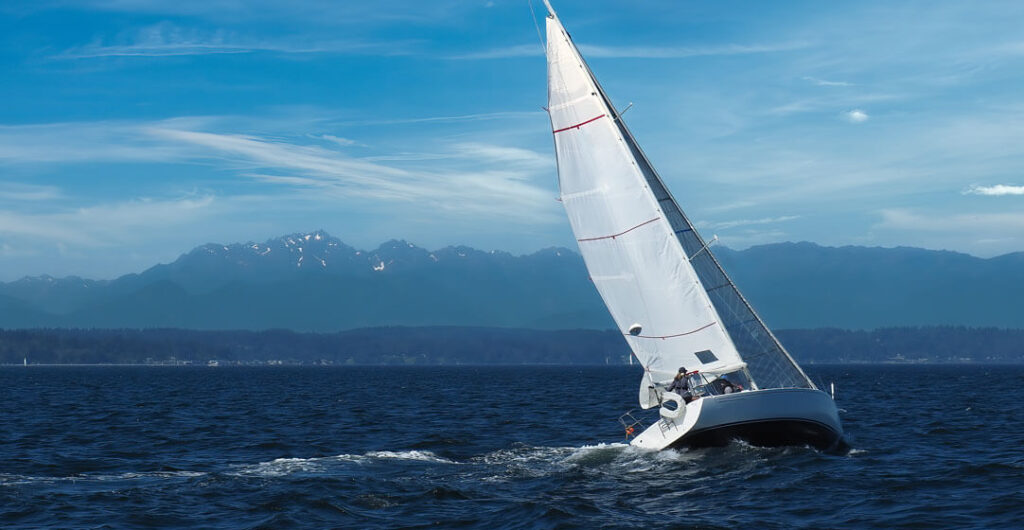 A sailboat cruises on Elliott Bay with the Olympic Mountains in the background. Almost all types of boats should be covered by boat insurance, including large sailboats.