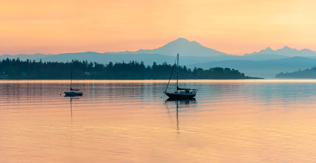 Boats at daybreak on the water with an orange background to illustrate the importance of boat insurance.