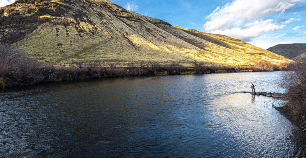 Wild rivers are ideal for fly fishing. A solitary fisherman stands on a spit on the Yakima River while fly fishing. 