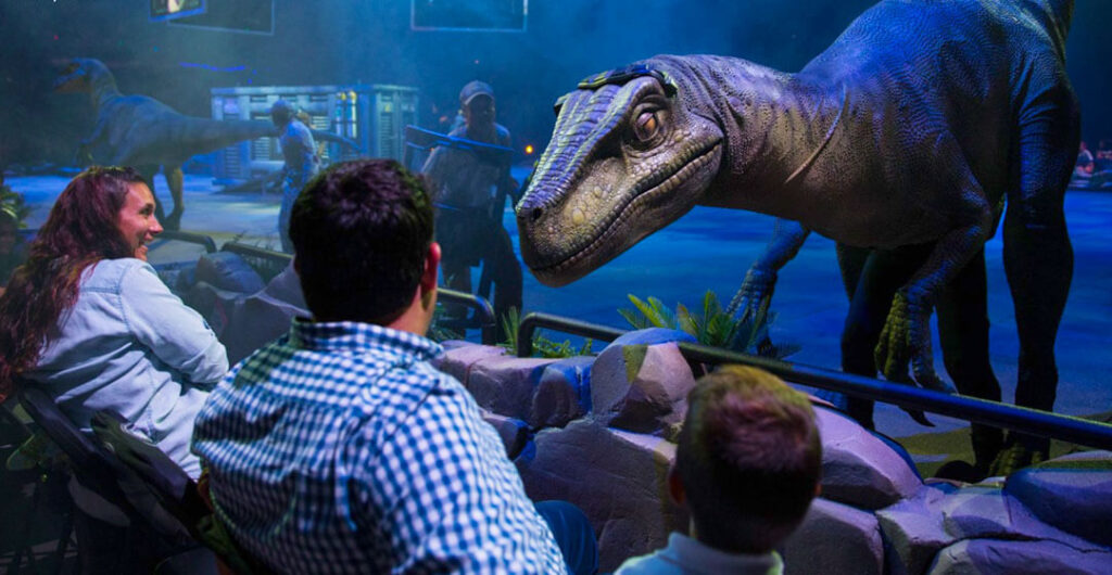 A velociraptor approaches two people at Jurassic World live