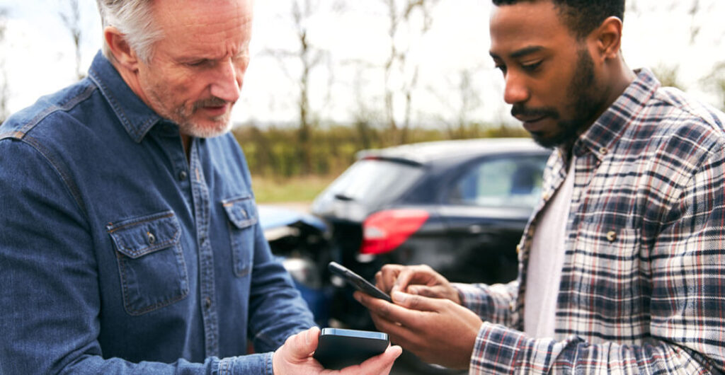 Two men exchange information on their cellular phones after an accident, to illustrate the need for robust levels of car insurance. 