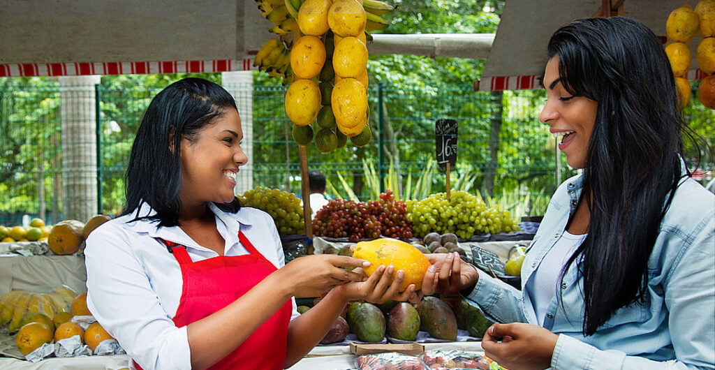 A woman buys a mango while abroad to illustrate foreign currency exchange 