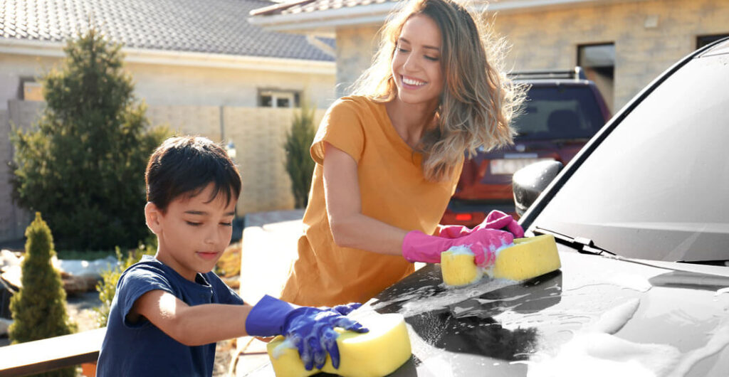 A woman washes her car with the help of her young son, to illustrate the importance of umbrella insurance. 