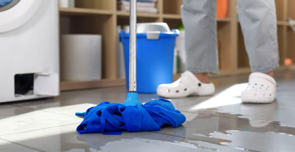 A photo of a broom mopping up a flooded basement from a washing machine, to illustrate water damage coverage in home insurance policies