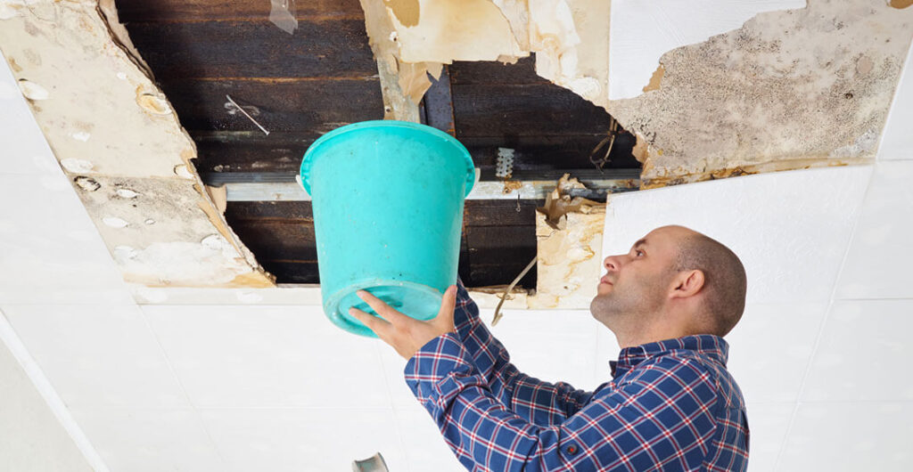 A man collects water through a hole in the ceiling caused by water damage. 