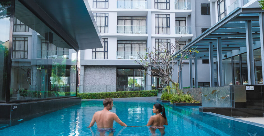 A man and a woman hold hands in the pool of their condo complex, to illustrate the importance of condo insurance. 