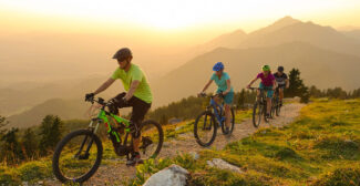 Three riders on e-bikes are riding in the mountains at sunset, to illustrate e-bikes.