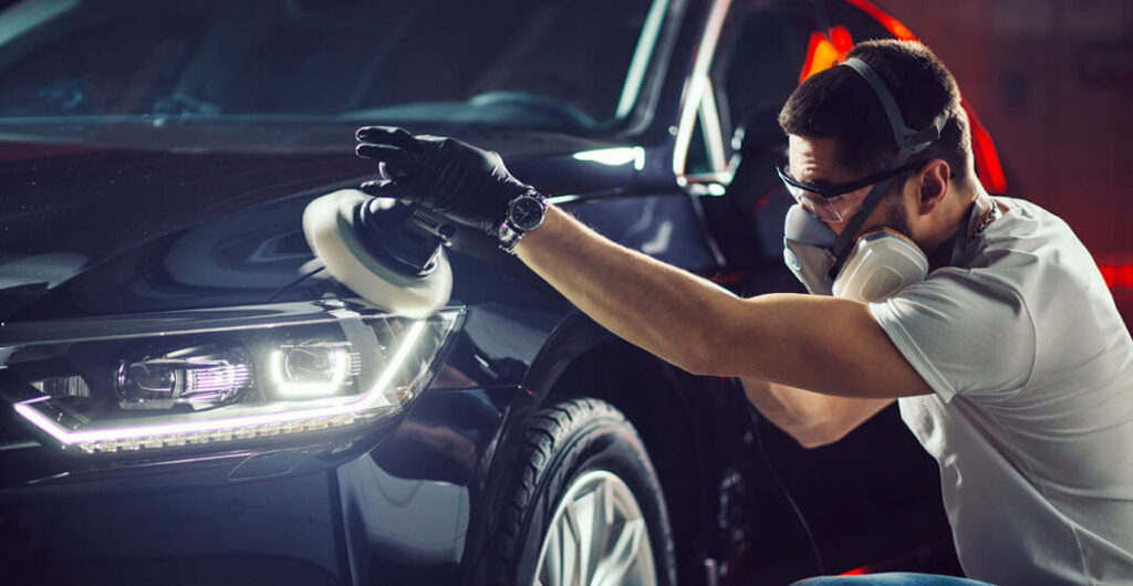 A man leans over to buff a car with a hand tool, to illustrate that AAA members in the Puget Sound area can get a generous car discount on detailing services. Photo: alfa 27/AdobeStock