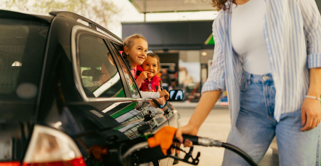 Two little girls peek out the window while their mom fills up the gas tank, to illustrate that AAA Washington members can get a discount on gas at Shell stations.