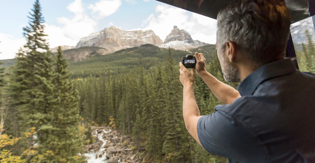 A man snaps a photo of rocky peaks from the open-air viewing platform on the Rocky Mountaineer.